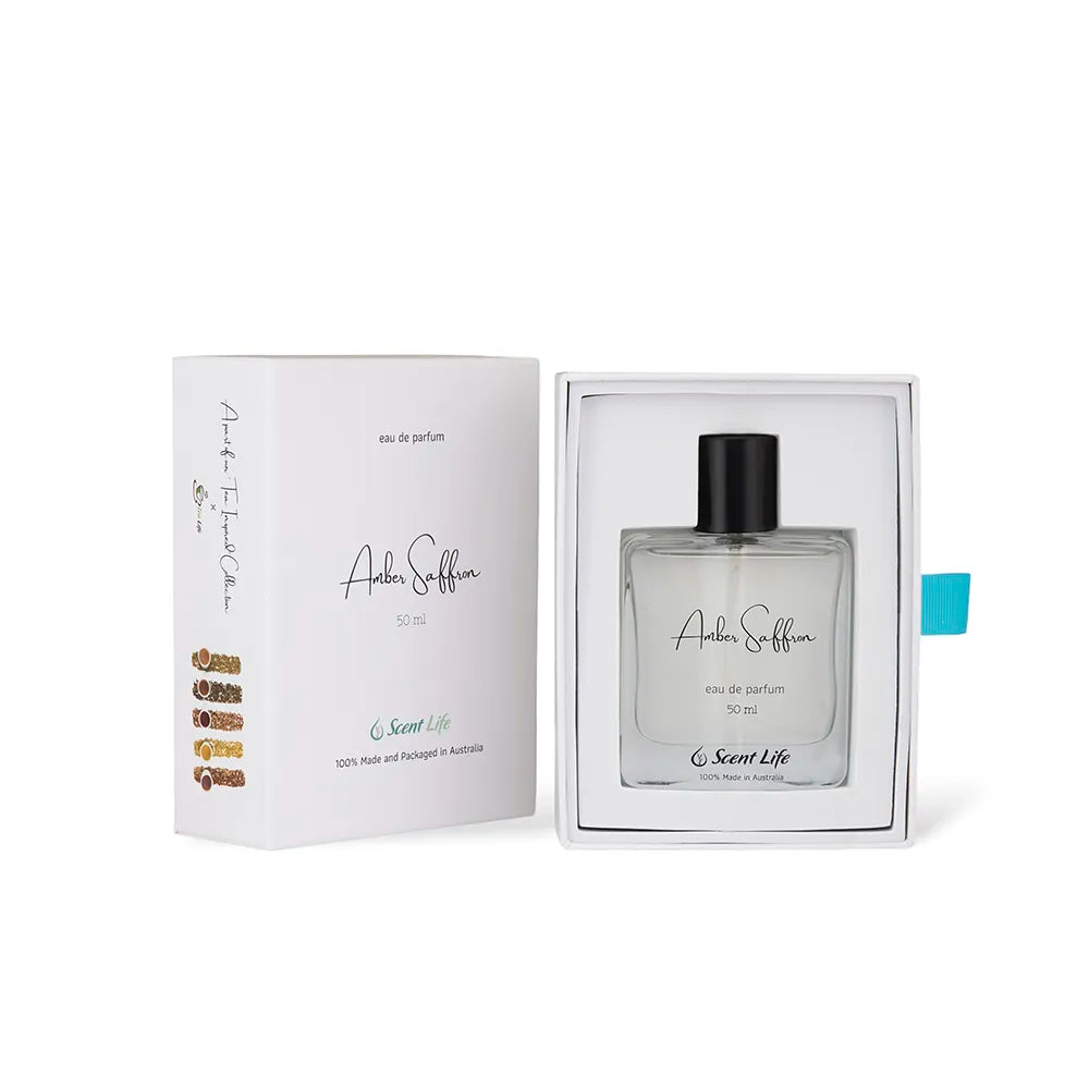 A 50 ml bottle of Scent Life's Amber Saffron eau de parfum is presented in an open white box. The packaging boasts elegant black and gold text, accented by a blue-green tab on the side, subtly evoking notes of Green Tea Jasmine.