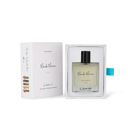 A bottle of Scent Life's Manuka Memories eau de parfum, exuding a honeyed sweetness, sits elegantly in an open white box. The perfume bottle features a simple design with a black cap, and the box is tastefully adorned with elegant text and a light blue ribbon.