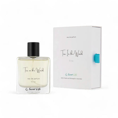 A 50 ml bottle of Scent Life's Tea in the Woods eau de parfum is displayed alongside its sophisticated packaging. The bottle, featuring a black cap, reveals the pale yellow fragrance within. Experience this enduring scent, elegantly presented in white packaging adorned with blue and black accents.